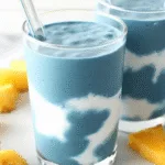 blue spirulina smoothie in a glass with fruit on white marble background
