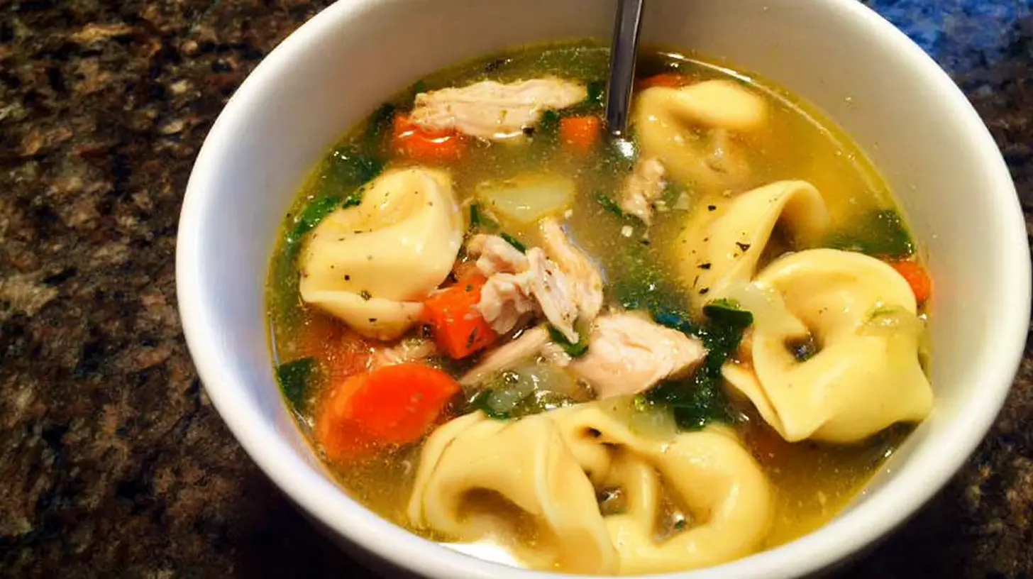 Close-up of a hearty bowl of easy tortellini soup with chicken, carrots, and spinach.