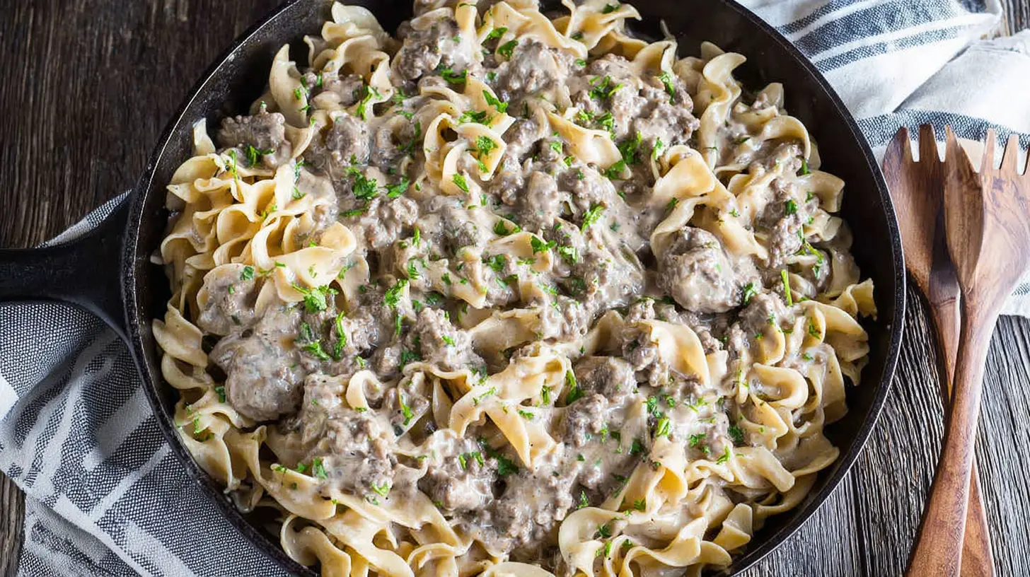 Overhead view of a hearty ground beef stroganoff in a cast-iron skillet, garnished with fresh herbs.
