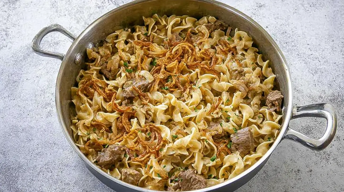 Creamy French Onion Beef and Noodles: Your New One-Pot Favorite French Onion Beef and Noodles Hearty French Onion Beef and Noodles dish in a shiny metal pan, topped with crispy fried onions and fresh herbs.